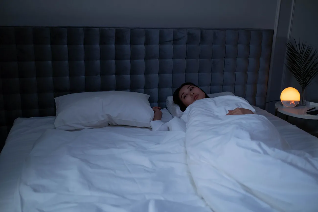 Man asleep in a dark bedroom, one of many people who sleep hot